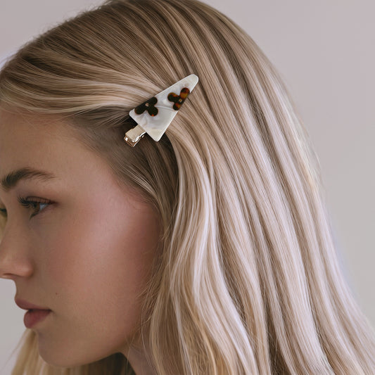 A close-up side profile of a woman with long blonde hair wearing a white tortoiseshell hair clip with dark brown accents.