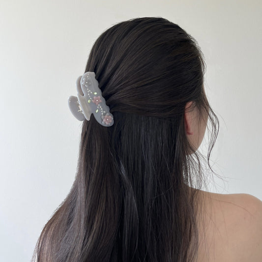 Person with long dark hair wearing a floral design hair claw clip on a plain background