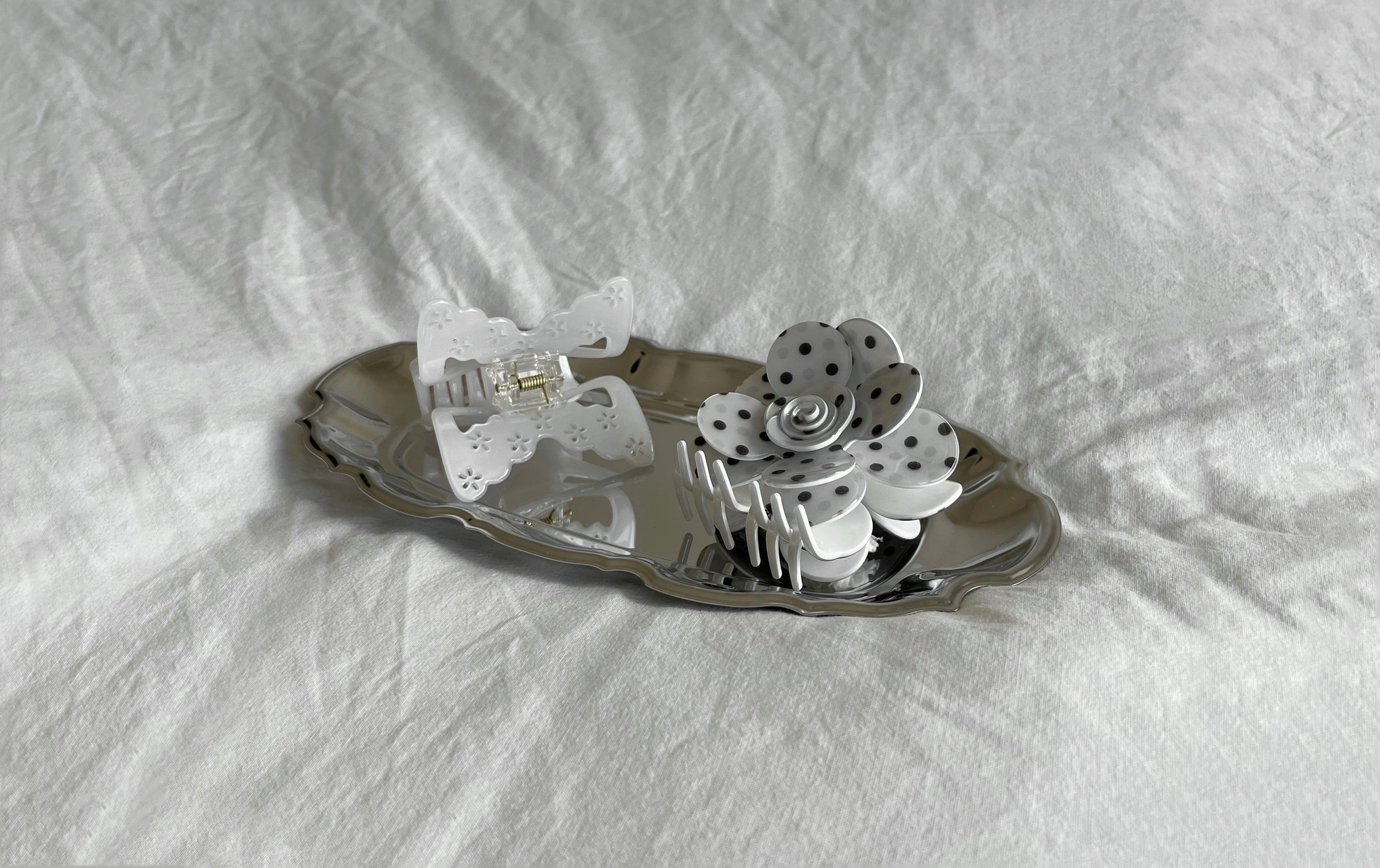 Butterfly claw clip and polka dot flower claw clip in a silver tray on white sheet