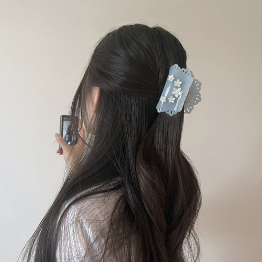 Girl with long dark hair wearing a lace cutout blue hair claw clip with pearl white floral decoration against a plain background