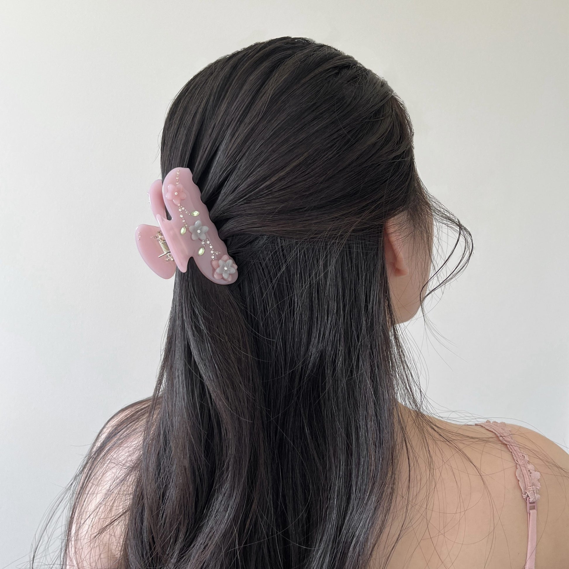 Person with long dark hair wearing a pink hair claw clip with flower design in half-up hairstyle against a plain background