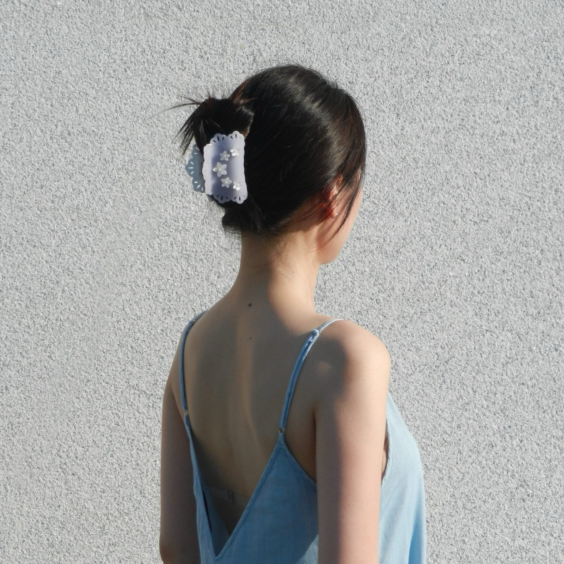 Woman wearing a blue dress and a lavender gray lace edge hair claw clip with floral decor in a textured gray wall background